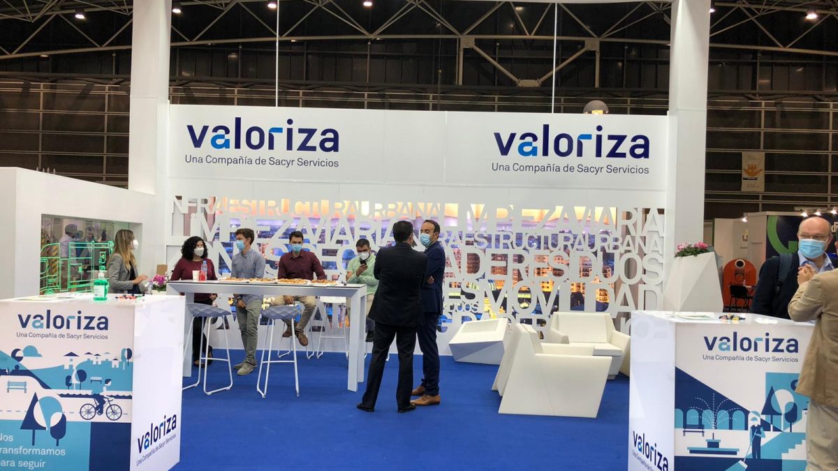 Stand de una empresa en una feria, con varias personas sentadas en una mesa y dos de pie conversando