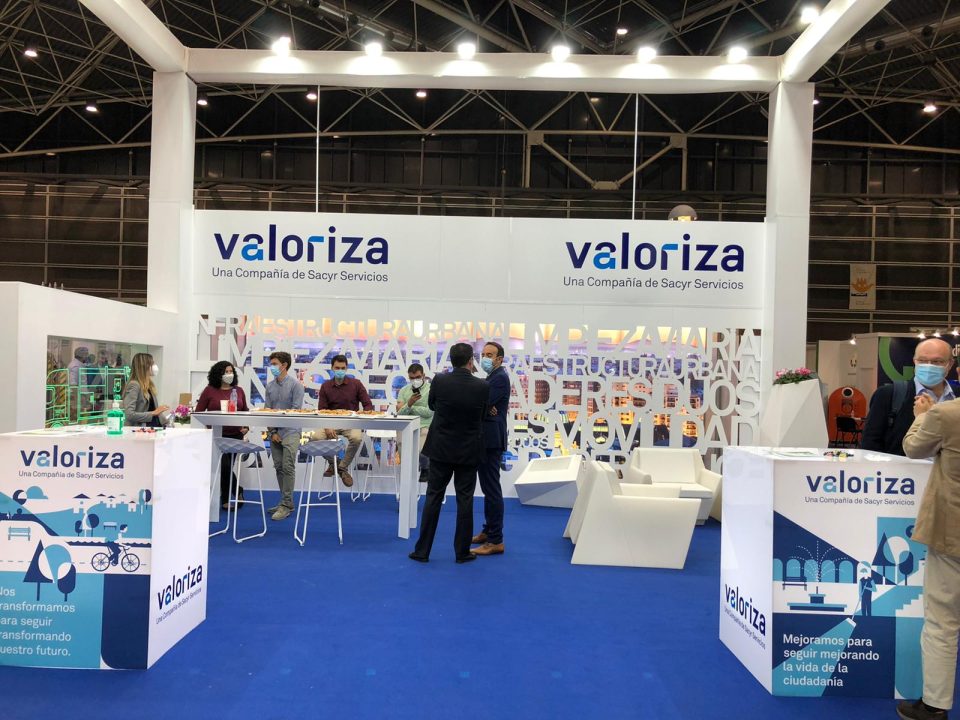 Stand de una empresa en una feria, con varias personas sentadas en una mesa y dos de pie conversando