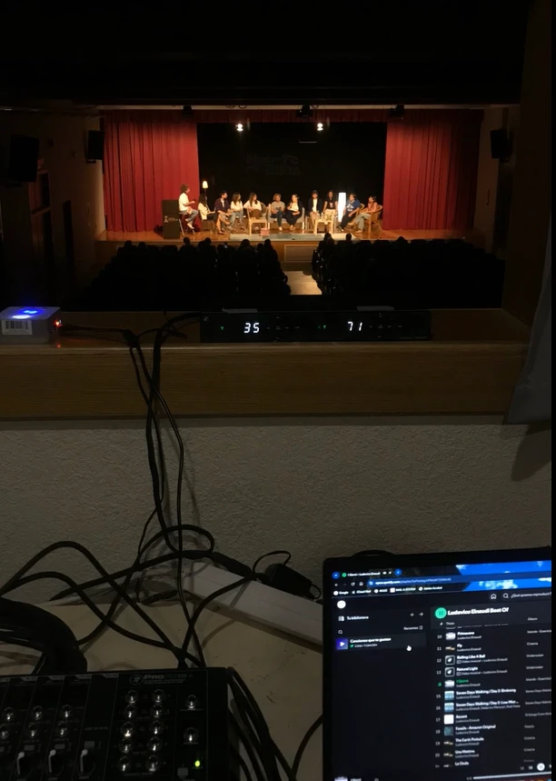 Portátil con Software profesional y mesa de sonido con escenario al fondo.