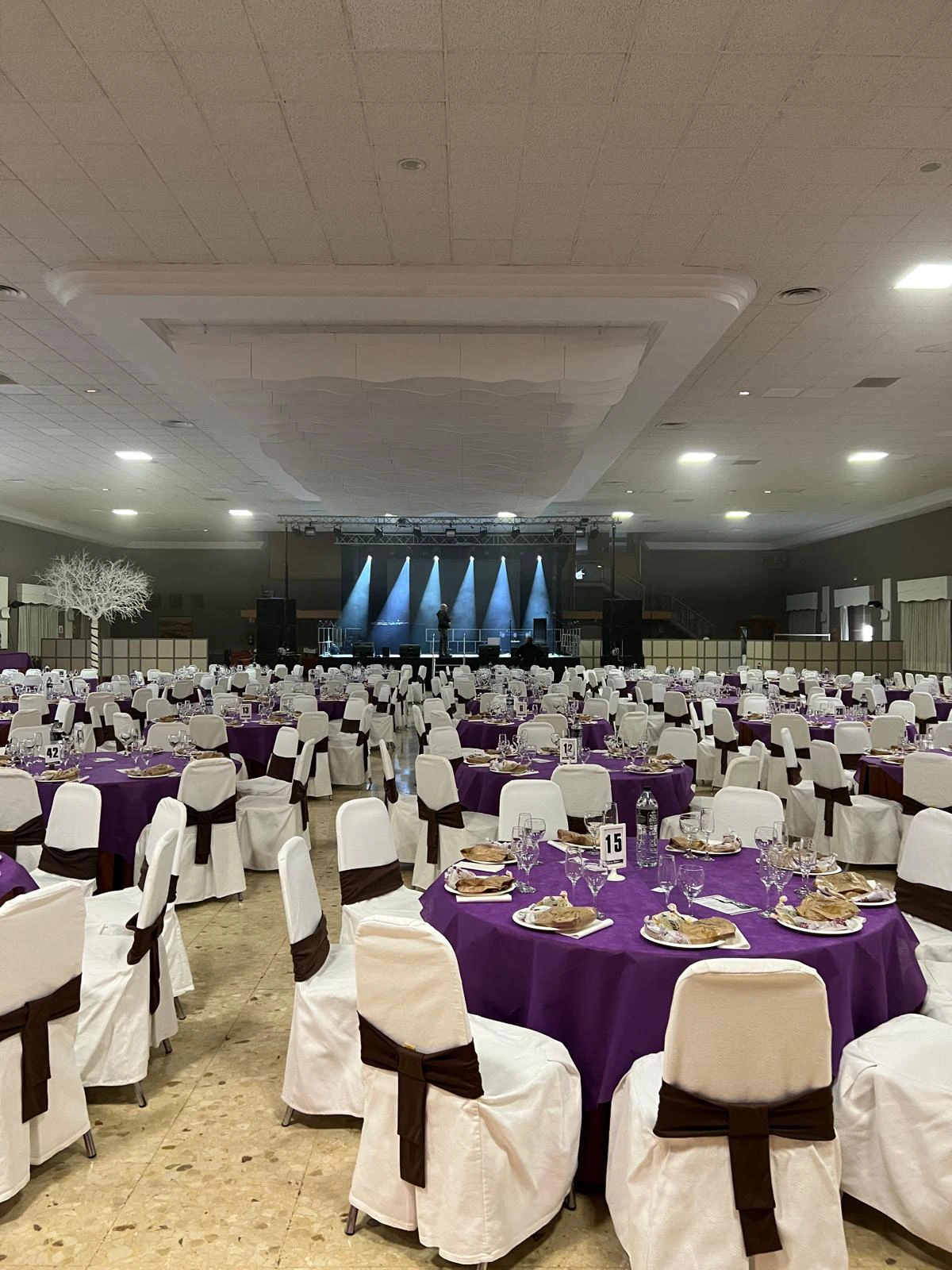 Evento en amplio salón con mobiliario de mesas y sillas y un escenario al fondo