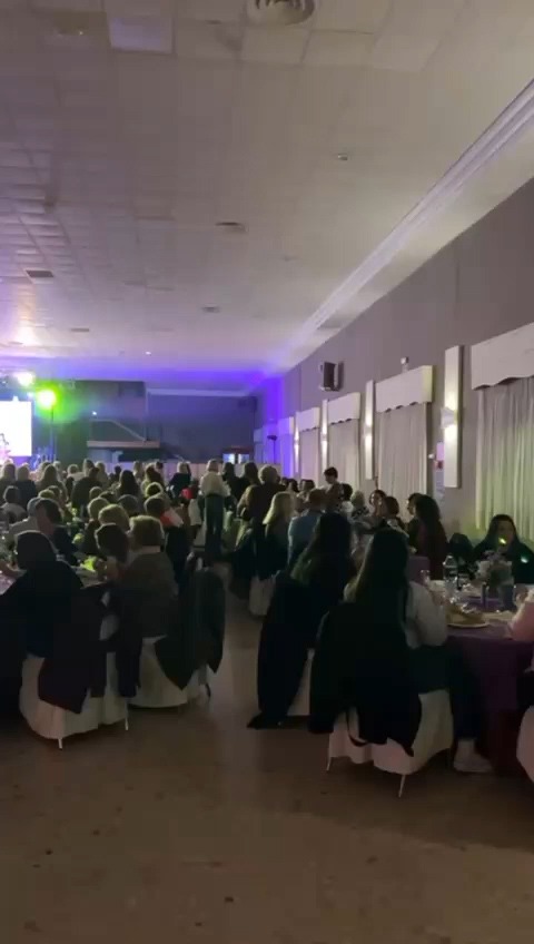 Evento en amplio salón con gran asistencia de público y una pantalla al fondo